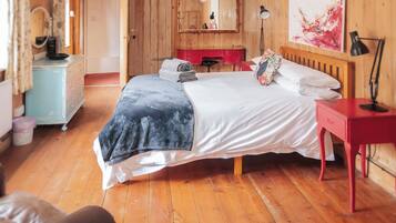 A wooden-paneled room with a bed, a red nightstand, a mirror, and a painting on the wall.