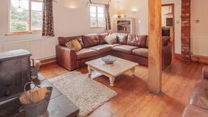 Una sala de estar acogedora con un sofá de cuero marrón, una mesa de centro de madera, una chimenea y una cocina rústica visible a través de un vano abierto.