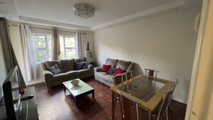 A living room with a sofa, a coffee table, and a dining table with chairs. There is a chandelier on the ceiling.