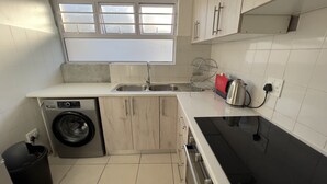 A compact kitchen with a washing machine, a sink, a kettle, and a stove.