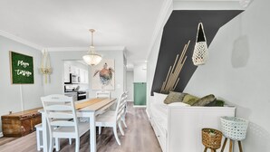 Ein modernes Wohnzimmer mit einem weißen Sofa, einem Esstisch mit weißen Stühlen, einer Küche im Hintergrund und einer Treppe mit schwarzem Akzentwand.