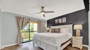 Ein Schlafzimmer mit Bett, Deckenventilator, Nachttisch, Lampe und Blick ins Freie.