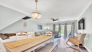 Ein moderner, hell erleuchteter Raum mit Esstisch, Bänken, einer Couch und einem Deckenventilator.