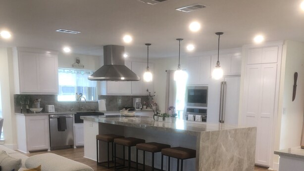 A modern kitchen with white cabinets, a central island with bar stools, and a dining area with a wooden floor. - Joy's Melissa House (Melissa)