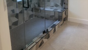 A modern bathroom with a glass shower enclosure, geometric patterned tiles, a small window, and a towel rack. - Joy's Melissa House (Melissa)