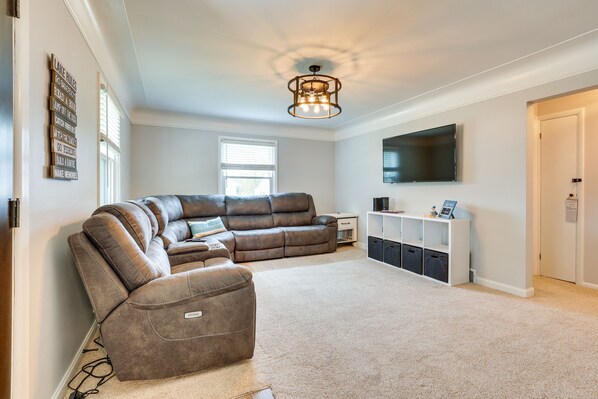 A modern living room with a sectional sofa, a flat-screen TV, and a ceiling light fixture. - Chippewa Lake Cottage w/ Fire Pit! (Chippewa Lake)