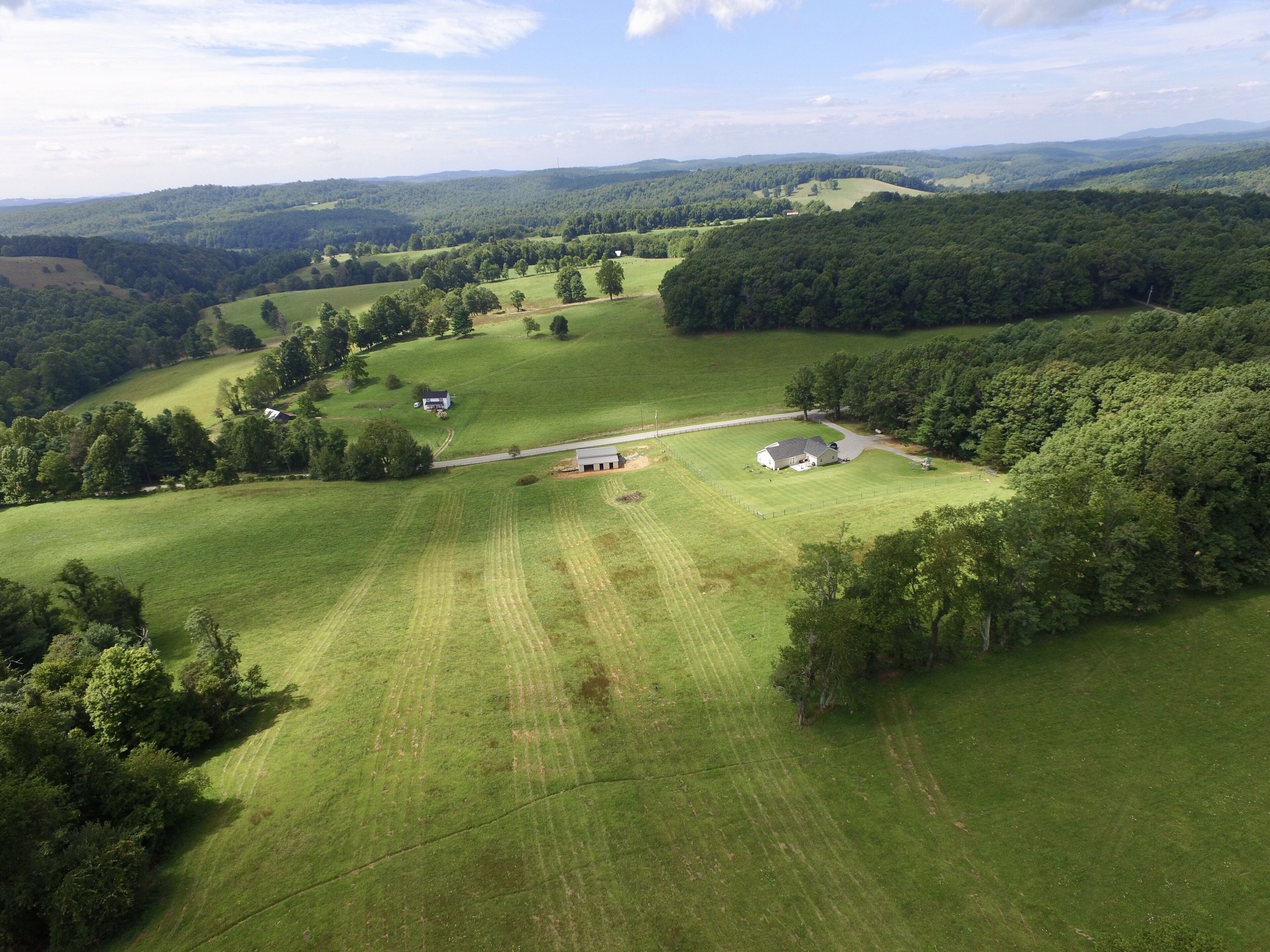 Vista aérea de un paisaje rural con colinas ondulantes, una casa de campo y campos circundantes.