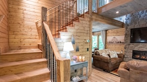 A wooden staircase with a railing, a fireplace, a sofa, and a coffee table in a cabin-style interior. - Treehouse, Hot Tub, Creekfront, Starlink Wi-Fi, Firepit (Franklin)