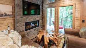 A cozy cabin interior with a stone fireplace, wooden walls, and a large wooden table. - Treehouse, Hot Tub, Creekfront, Starlink Wi-Fi, Firepit (Franklin)