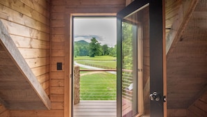 A wooden interior with a large open door leading to a balcony with a view of a green landscape and a winding path. - Treehouse, Hot Tub, Creekfront, Starlink Wi-Fi, Firepit (Franklin)