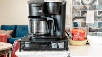 Una cafetera Keurig sobre una encimera blanca, con un tazón de café Folgers y una bolsa roja de café.