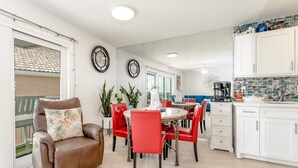 A modern kitchen with white cabinets, a dining area with red chairs, and a brown leather chair with a floral pillow.