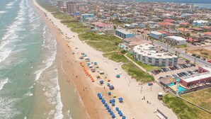 An aerial view of a coastal city with a long beach lined with umbrellas and buildings.