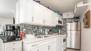 A modern kitchen with white cabinets, a stainless steel refrigerator, a coffee maker, and a tiled backsplash.