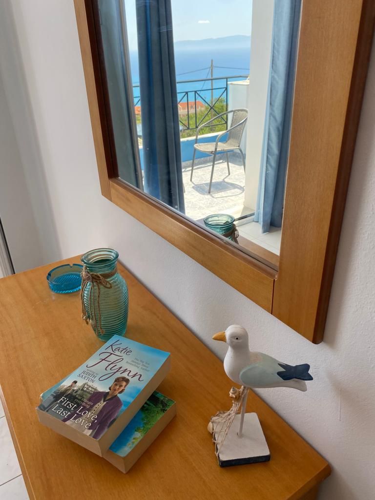 A room with a view of the sea, a wooden table with a book, a vase, and a bird figurine.