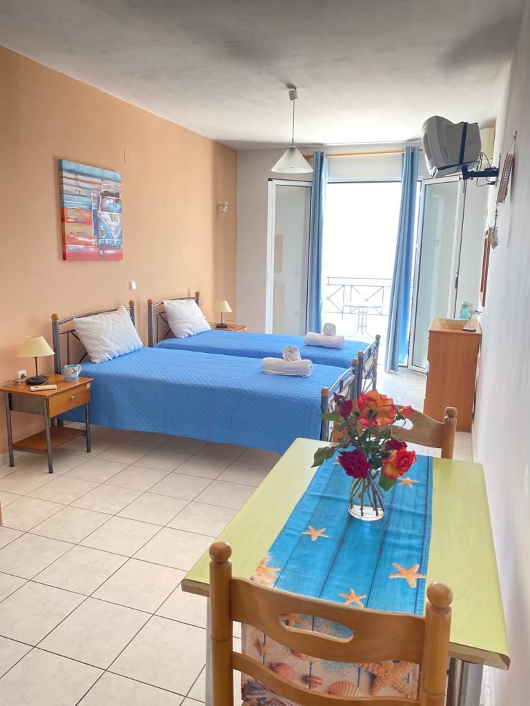 A hotel room with two beds, a dining table, a vase of flowers, and a balcony with a view.