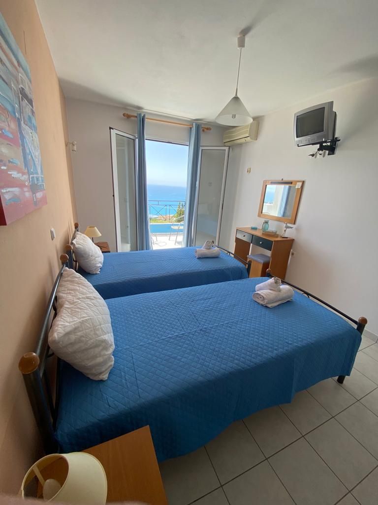 Habitación de hotel con dos camas, televisión, escritorio y vista al mar.