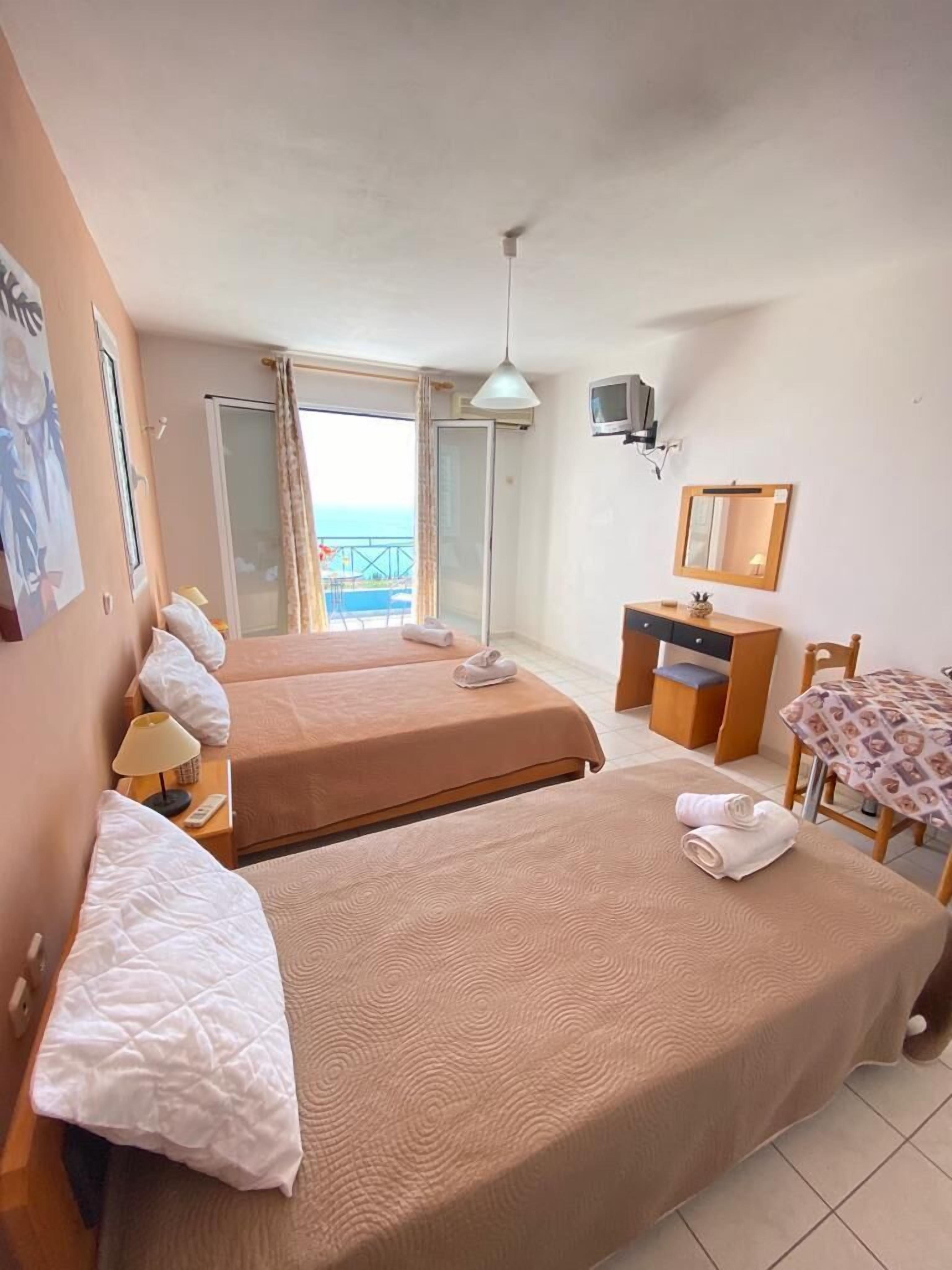 Ein Hotelzimmer mit zwei Betten, einem Schreibtisch, einem Sessel, einem Fernseher und einem Balkon mit Blick.