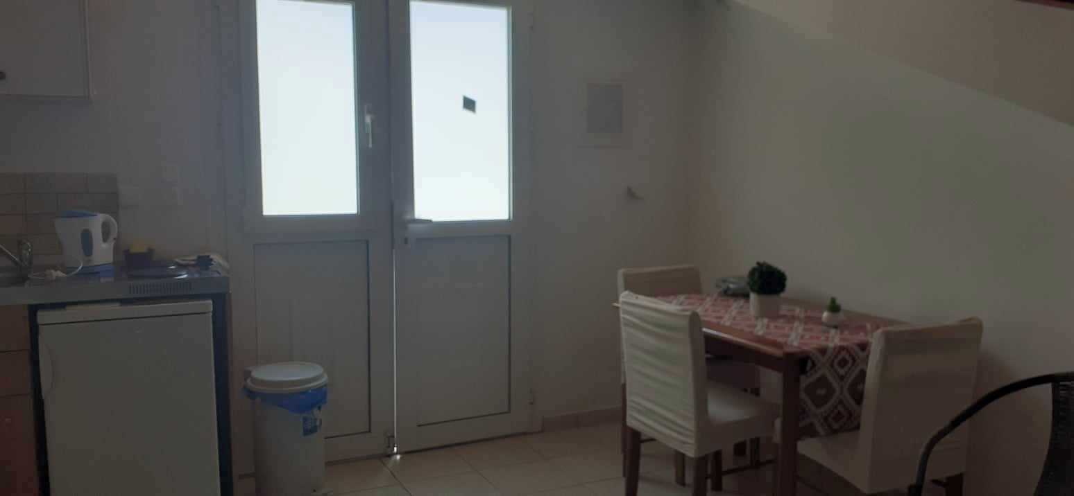 A compact kitchen with a refrigerator, a sink, and a window. There is a dining area with a table and chairs.