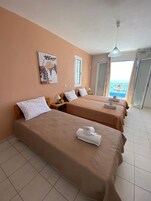 Habitación de hotel con dos camas, un cuadro en la pared y vista al mar desde el balcón.