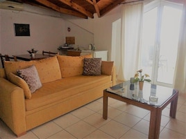 Una sala de estar con un sofá, una mesa de centro de vidrio y una cocina al fondo.