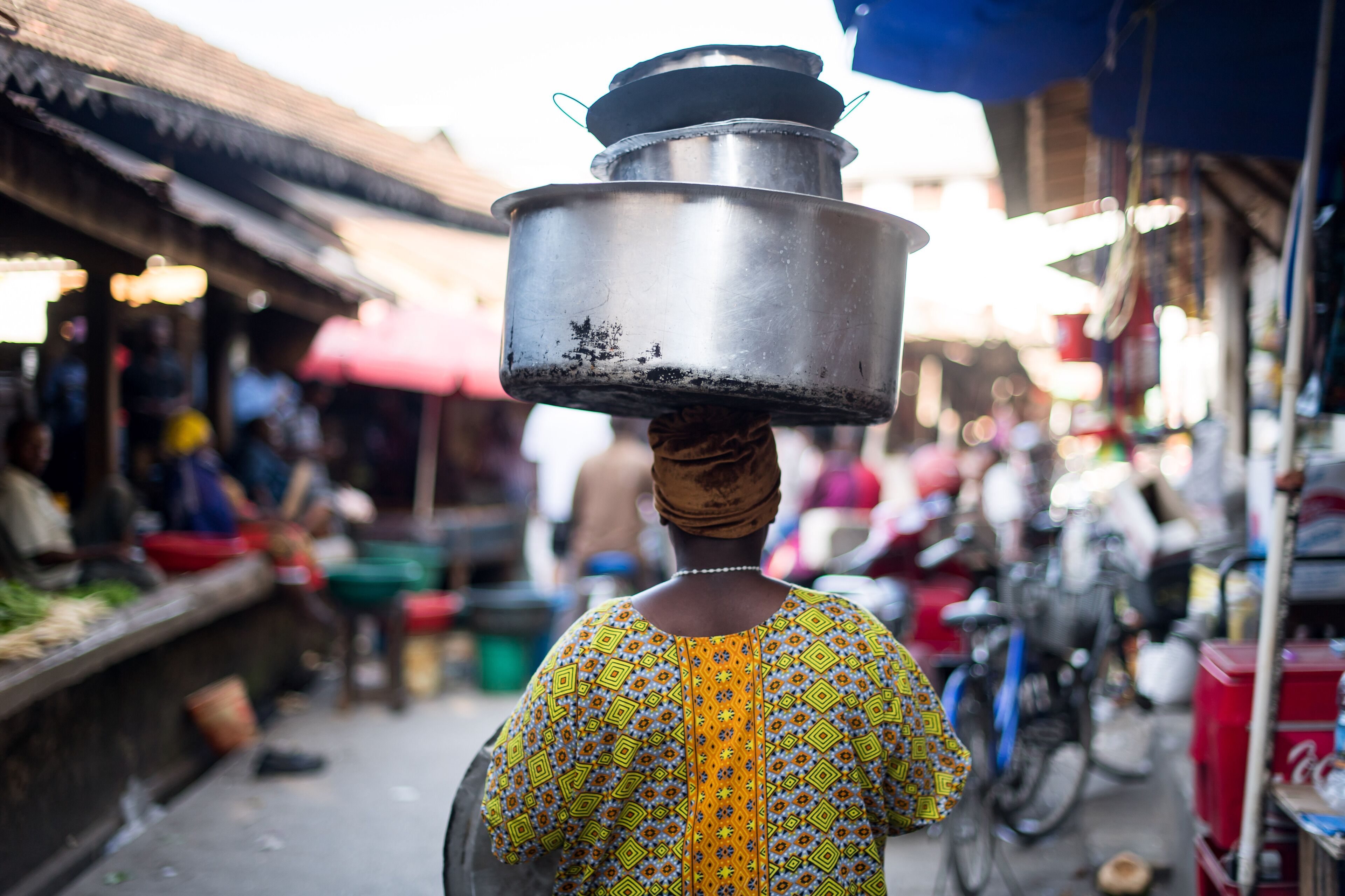 A person carrying a large pot on their head in a market setting.