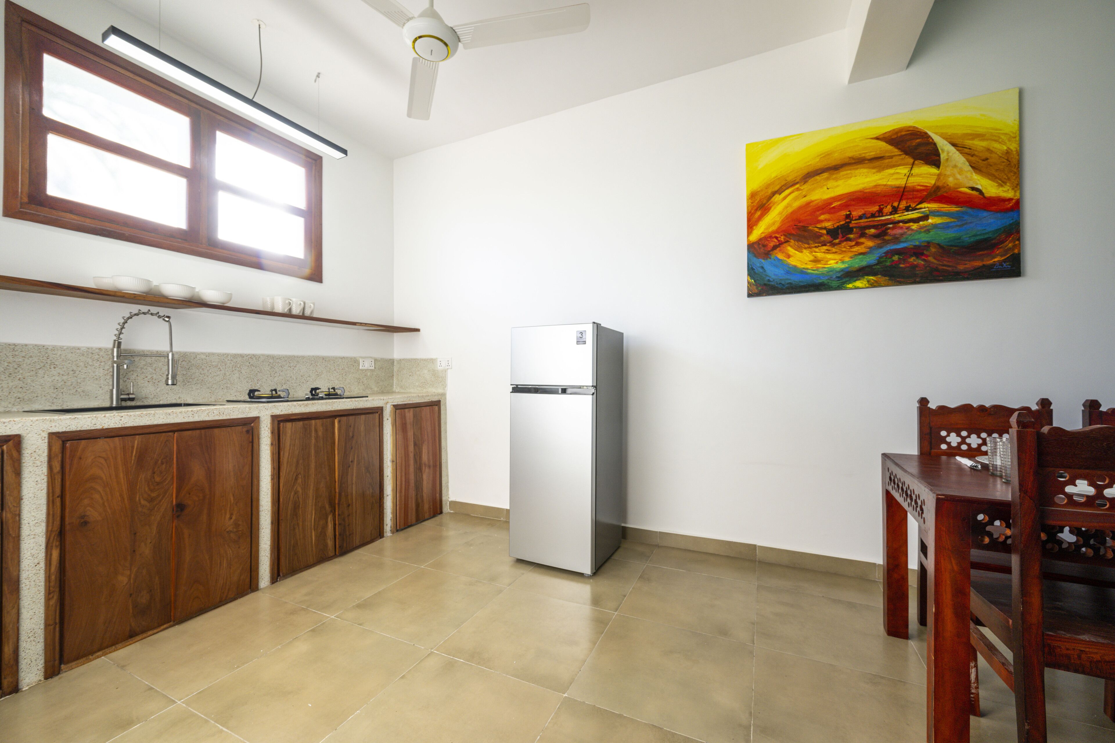 Una cocina con armarios de madera, un refrigerador de acero inoxidable y una zona de comedor con una mesa y sillas de madera.
