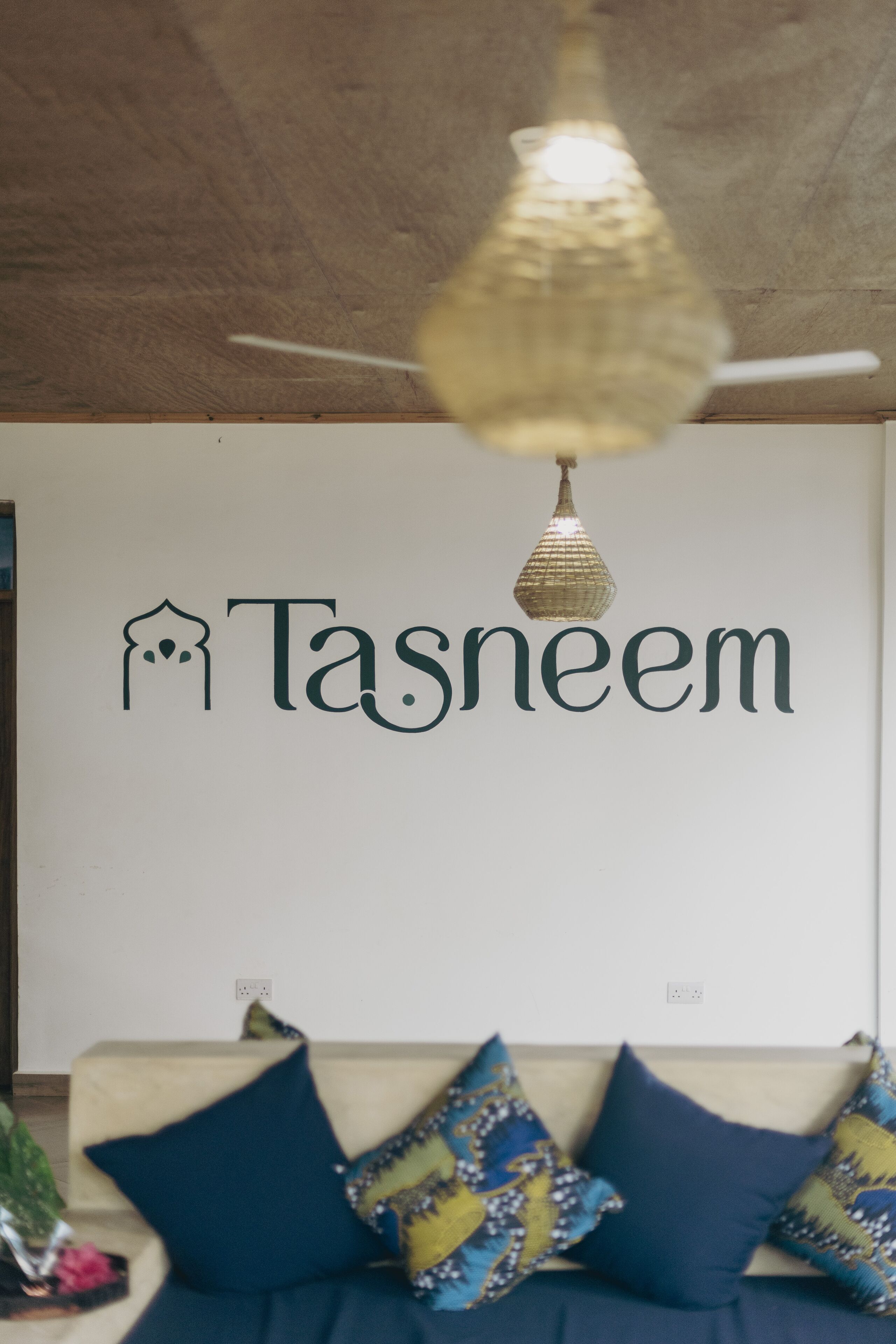 Egy fal, amelyen a „Tasneem” név szerepel, és egy díszlámpa.