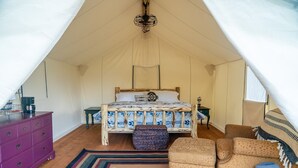 Una habitación con carpa, una cama, un aparador morado, un reposapiés estampado y una manta a rayas.