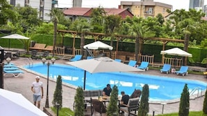 A swimming pool area with lounge chairs and umbrellas, surrounded by greenery and buildings in the background. - Hotel Genatsvale Batumi (Batumi)
