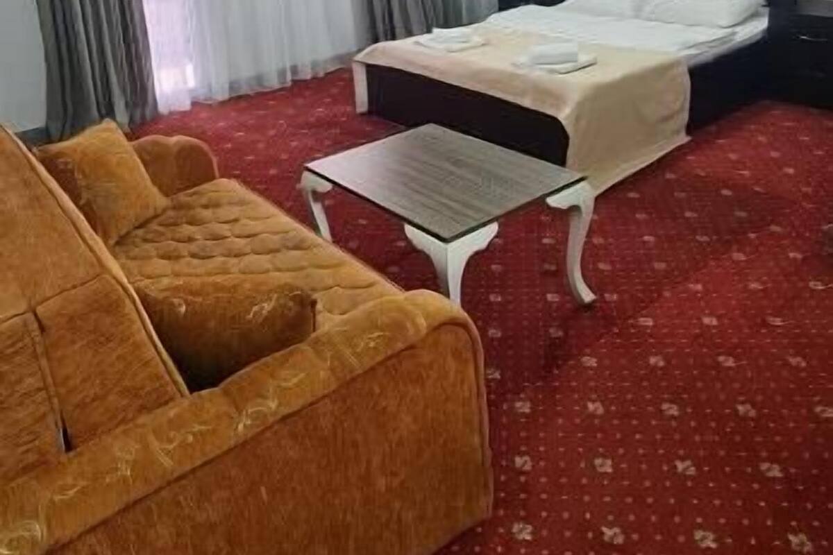 A hotel room with a bed, a sofa, a small table, and a window with curtains.