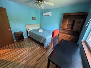 A bedroom with a bed, a desk, a chair, a wardrobe, a small bedside table, and a ceiling fan.