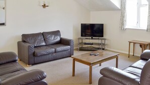 A living room with a grey leather sofa, a wooden coffee table, and a TV on a glass stand. - Pirates Cove - UK44493 (Hope Cove, near Kingsbridge)