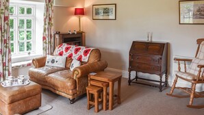 Un salon chaleureux avec un canapé en cuir, une table d’appoint en bois et un fauteuil à bascule. On peut également apercevoir une cheminée avec une lampe rouge et un tableau encadré accroché au mur.