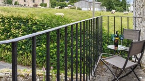 Un balcon avec une table et une chaise, donnant sur un champ verdoyant où paissent des moutons, avec un bâtiment en pierre en arrière-plan.