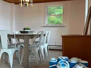 Un comedor con una mesa redonda y sillas blancas, una ventana que ofrece vistas al verdor y un atril de madera.