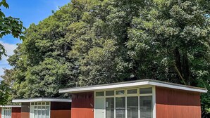 Two small, single-story buildings with large windows and a flat roof, surrounded by a well-maintained lawn and dense trees. - 2 bedroom accommodation in Cromer (Cromer)