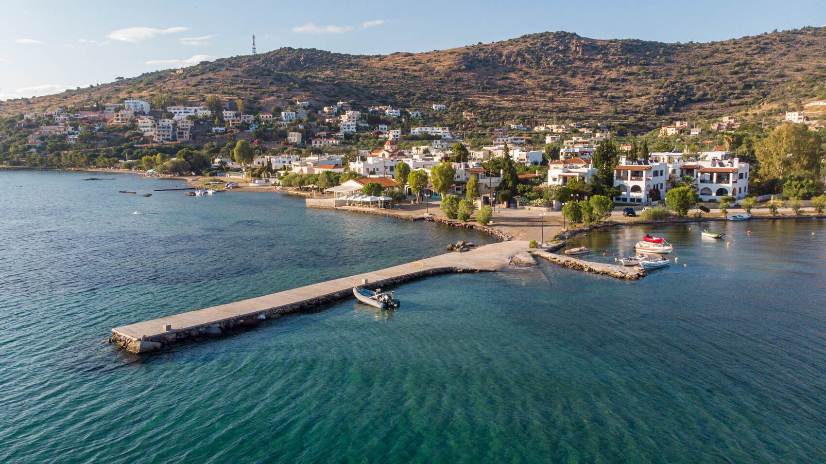Un pueblo costero con un muelle que se adentra en el mar, rodeado de edificios residenciales.