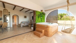 Een moderne woonkamer met een houten jacuzzi, een eethoek met rieten stoelen en uitzicht op groen.