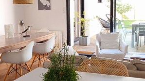 Uma sala de estar moderna com área de jantar, mobiliário branco e uma janela grande com vista para o exterior.