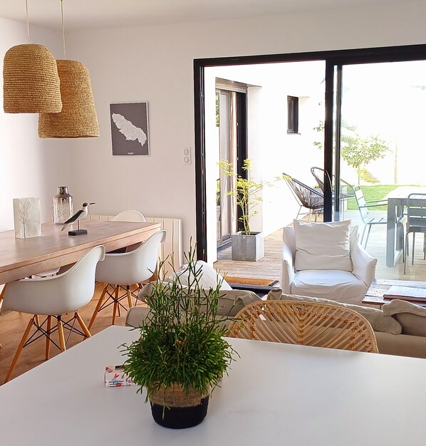 A modern living room with a dining area, white furniture, and a large window with a view of the outdoors.