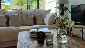 Uma sala de estar com sofá, mesa de centro com uma vela, um vaso com flores, luminária e televisão.