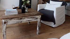 Uma sala de estar acolhedora com uma mesa de madeira rústica, uma poltrona confortável, uma lareira e uma estante de livros.