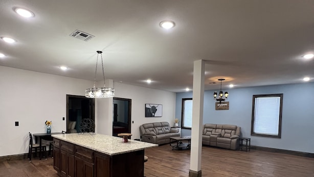 A spacious living room with a large wooden floor, a kitchen island with dark wood cabinets, and a dining area with a table and chairs.