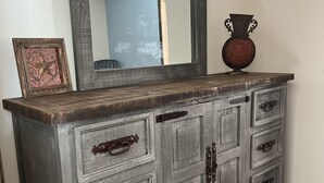 A wooden dresser with multiple drawers and metal handles, a mirror above it, and a vase on top.
