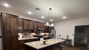 A modern kitchen with wooden cabinets, a granite countertop, and a central island with stools.