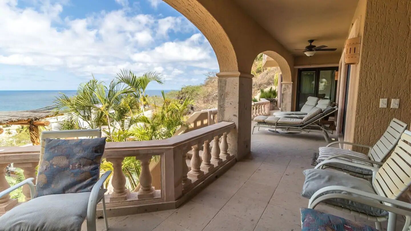A balcony with a view of the ocean, furnished with lounge chairs and a sofa.