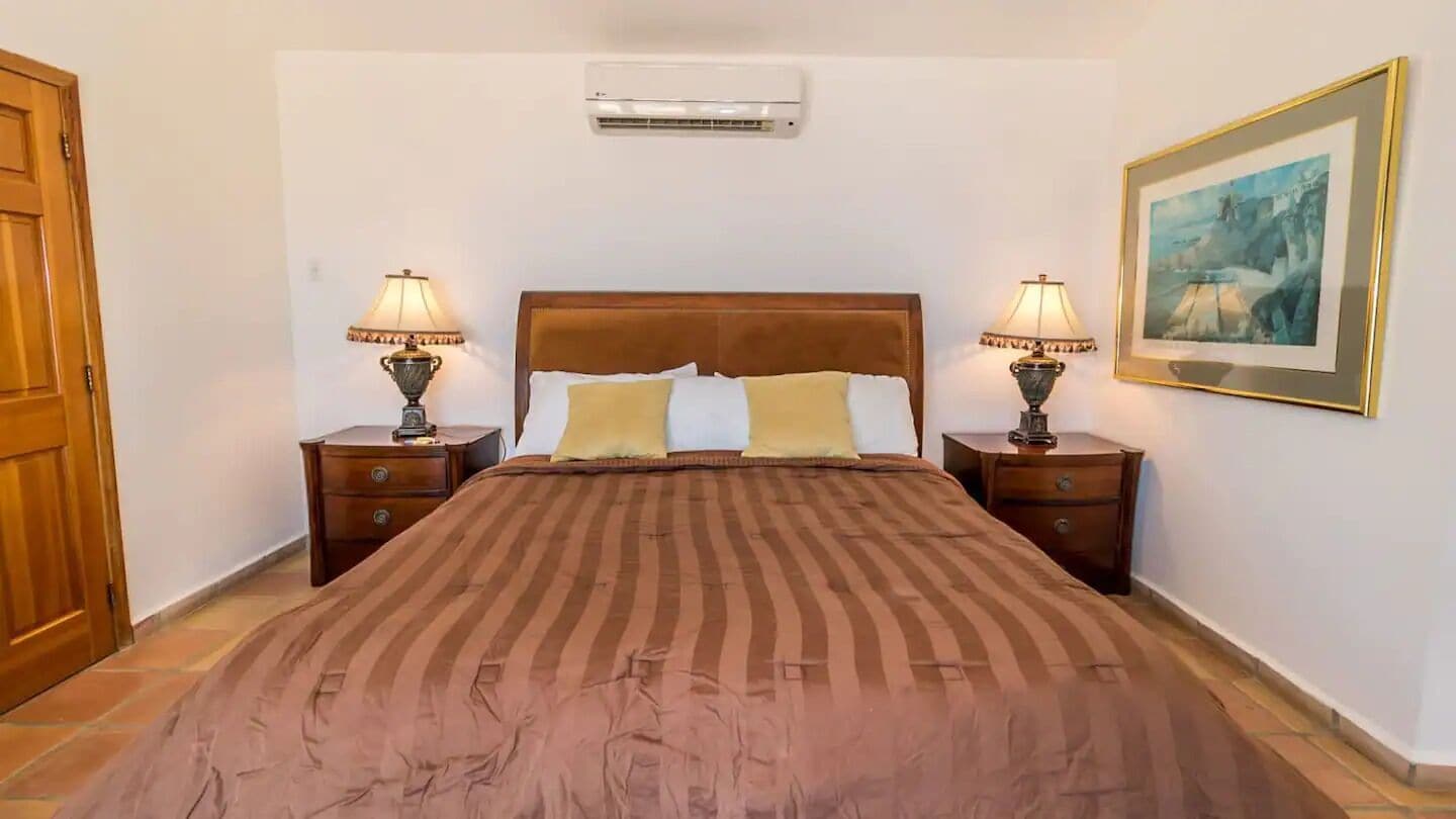 Une chambre d’hôtel avec un grand lit, deux tables de chevet avec des lampes, un climatiseur fixé au mur et un tableau encadré accroché au mur.