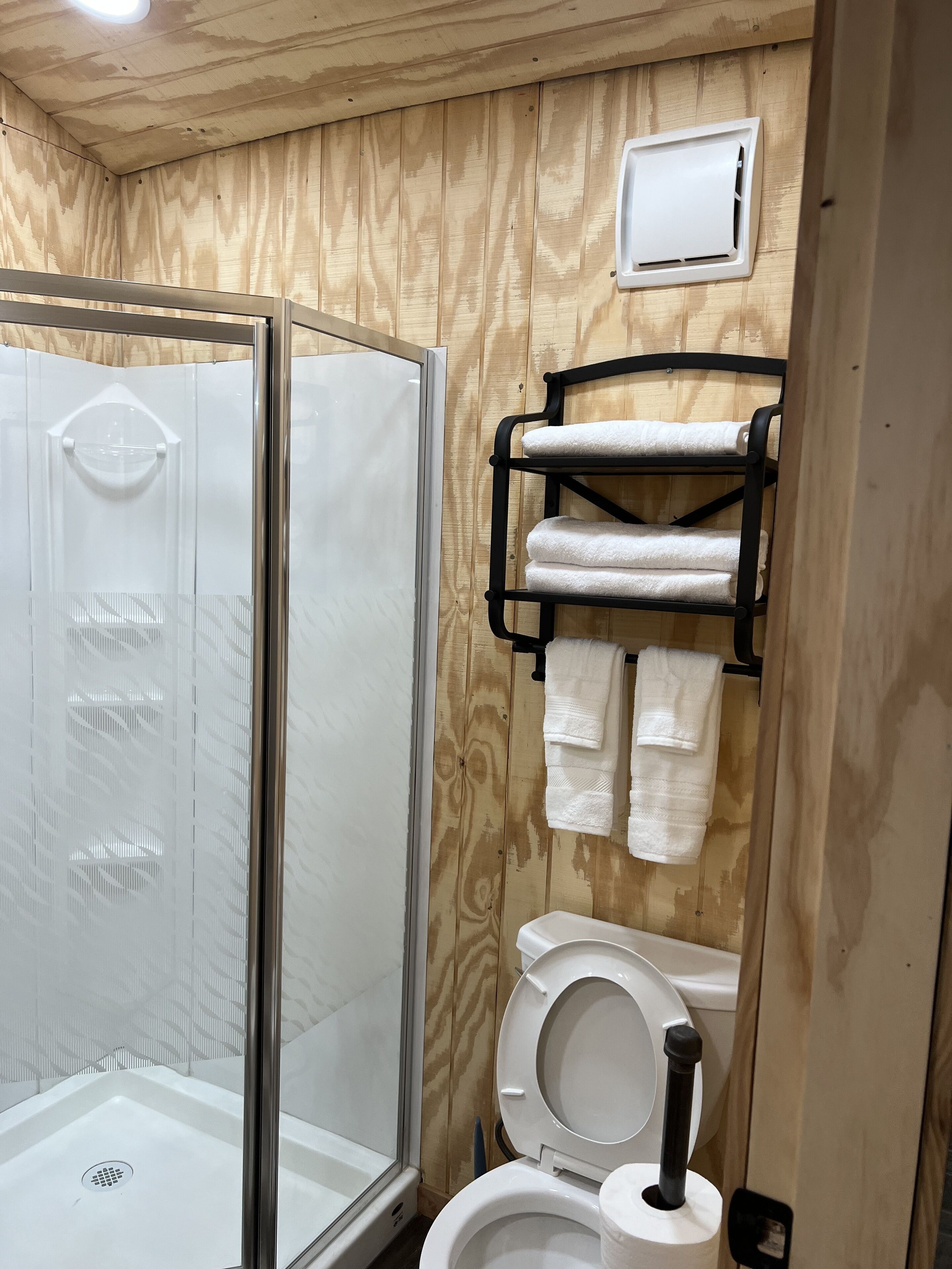 Un baño con ducha de vidrio, inodoro y toallero con toallas.