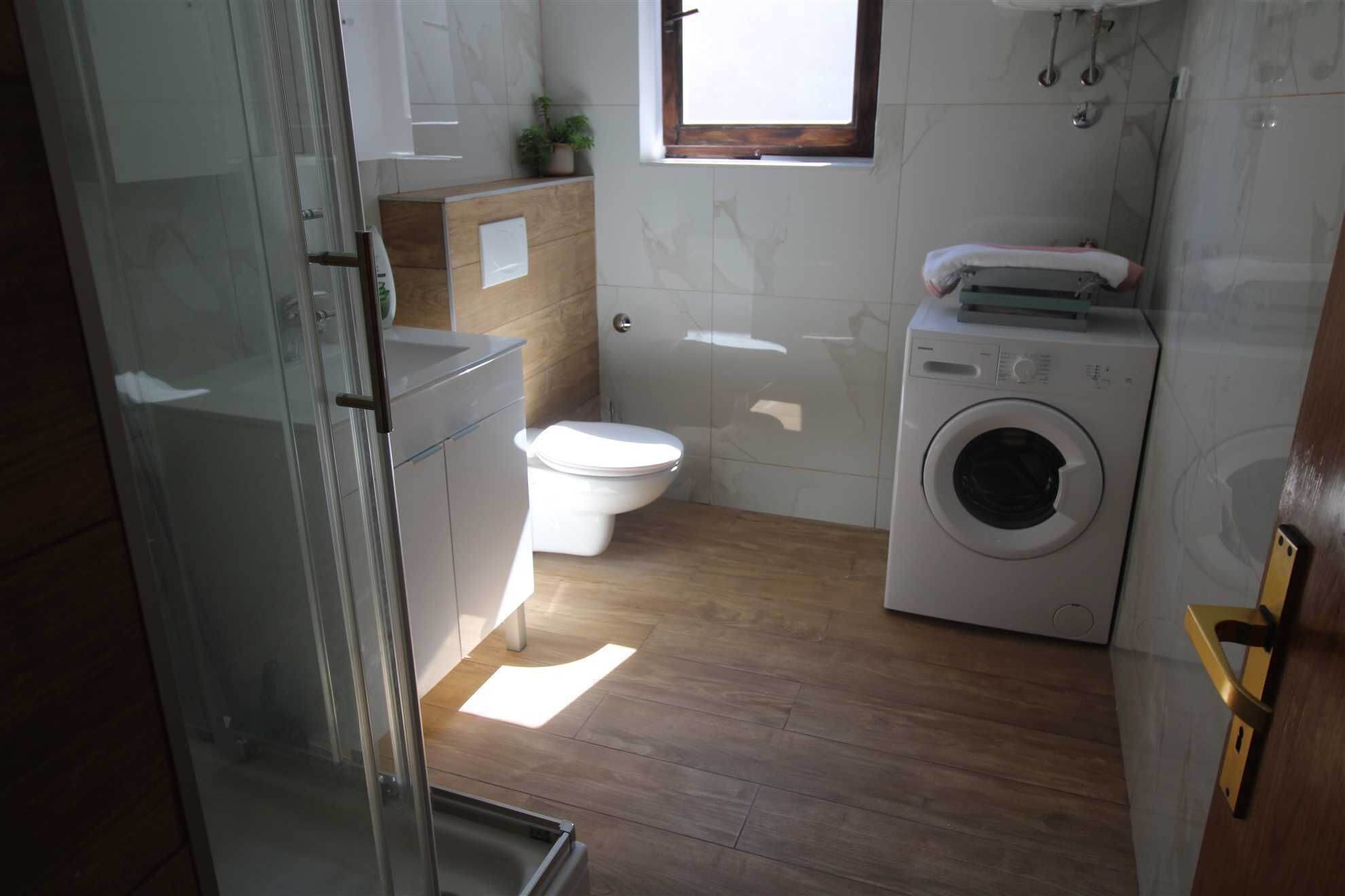 A small, compact bathroom with a toilet, washing machine, and a window.
